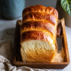 Loaf of light and fluffy Japanese milk bread with golden top and pull-apart sections on a wooden board
