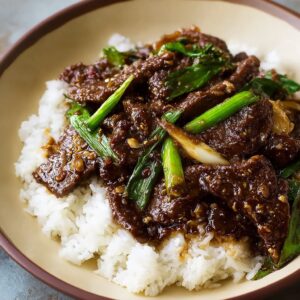Easy Mongolian beef recipe served over rice with sesame seeds and green onions