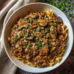 Healthy vegan lentil mushroom stroganoff in a bowl topped with fresh herbs and plant-based cream sauce