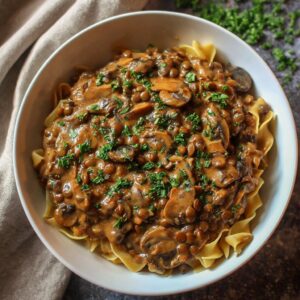 Healthy vegan lentil mushroom stroganoff in a bowl topped with fresh herbs and plant-based cream sauce