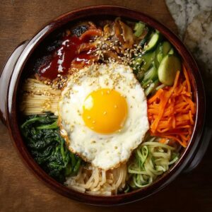 Bibimbap Korean rice bowl in a stone dol sot with marinated beef bulgogi, sautéed spinach, carrots, mushrooms, bean sprouts, fried egg, and gochujang sauce