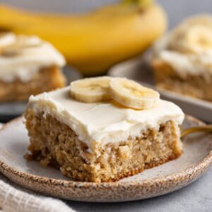Banana bars cut into squares with thick fluffy cream cheese frosting, golden moist banana cake, and chopped walnuts on top