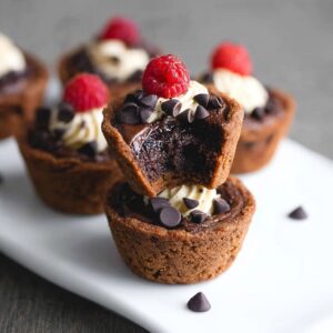 Bite-sized brownie tarts with fudgy chocolate cups, glossy chocolate ganache filling, fresh raspberry, and gold leaf garnish