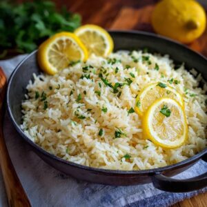 Lemon rice pilaf in a serving bowl, fluffy long-grain basmati flecked with lemon zest, golden toasted slivered almonds, chopped parsley, lemon wedges, butter pat melting