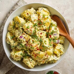 Classic potato salad in a white serving bowl, tender chunks of waxy potato coated in creamy dressing, diced hard-boiled egg, celery, dill pickle, red onion, fresh dill, paprika dusting