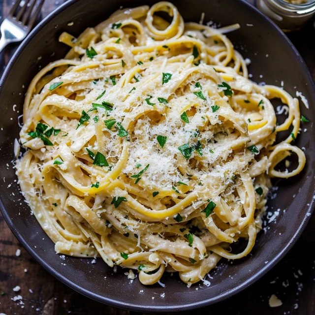 Close-up of aglio e olio linguine showing al dente pasta glistening with olive oil, slivers of toasted garlic, bright green parsley, red chili flakes scattered, parmesan dusting on top