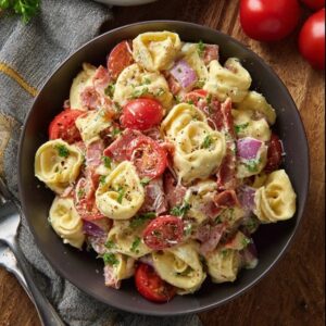 Tortellini salad with bacon in a large white serving bowl, plump cheese tortellini tossed with crispy bacon pieces, fresh baby spinach leaves, halved cherry tomatoes, sliced red onion, shredded parmesan, glossy Italian vinaigrette dressing coating everything, fresh basil leaves on top