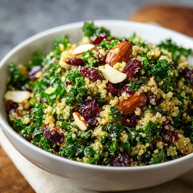 Quinoa kale salad in a ceramic bowl, fluffy tri-color quinoa with massaged green kale leaves, ruby red dried cranberries scattered, crumbled white feta cheese, golden almond slivers, lemony vinaigrette dressing