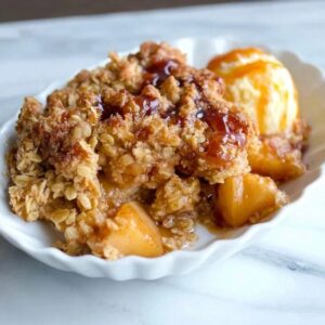 Apple crisp in a baking dish with golden bubbly streusel topping over cinnamon apples, scoop of vanilla ice cream melting on top, caramel drizzle, fall light