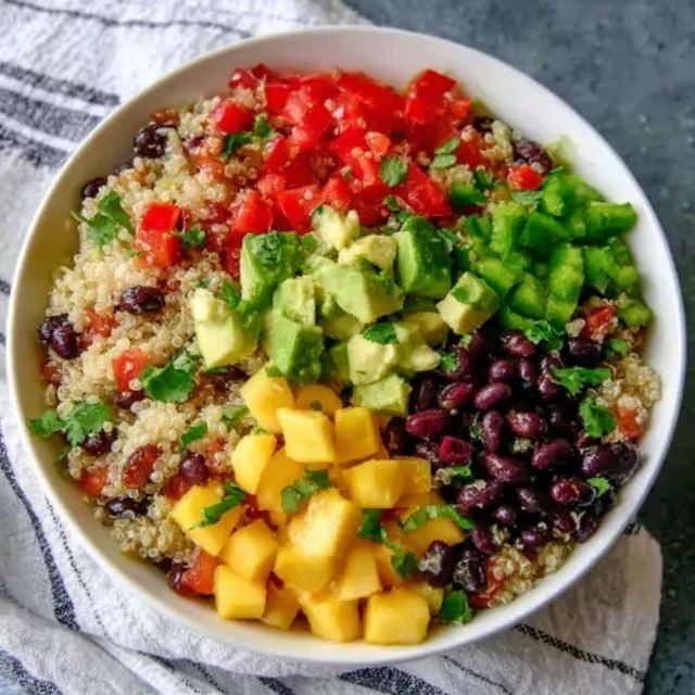 Close-up of colorful salad showing tiny grains of quinoa, mango chunks glistening, black beans, red bell pepper, cilantro leaves, ranch of color