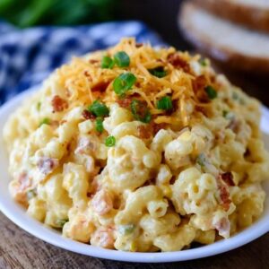 Cheesy bacon macaroni salad in a bowl, elbow macaroni in a creamy dressing with cubes of cheddar, crispy bacon bits, diced celery and red onion, sprinkle of chives