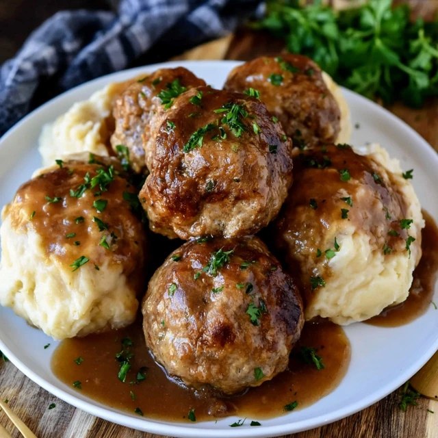Close-up of a meatball cut open over mashed potatoes with brown gravy pooling around it