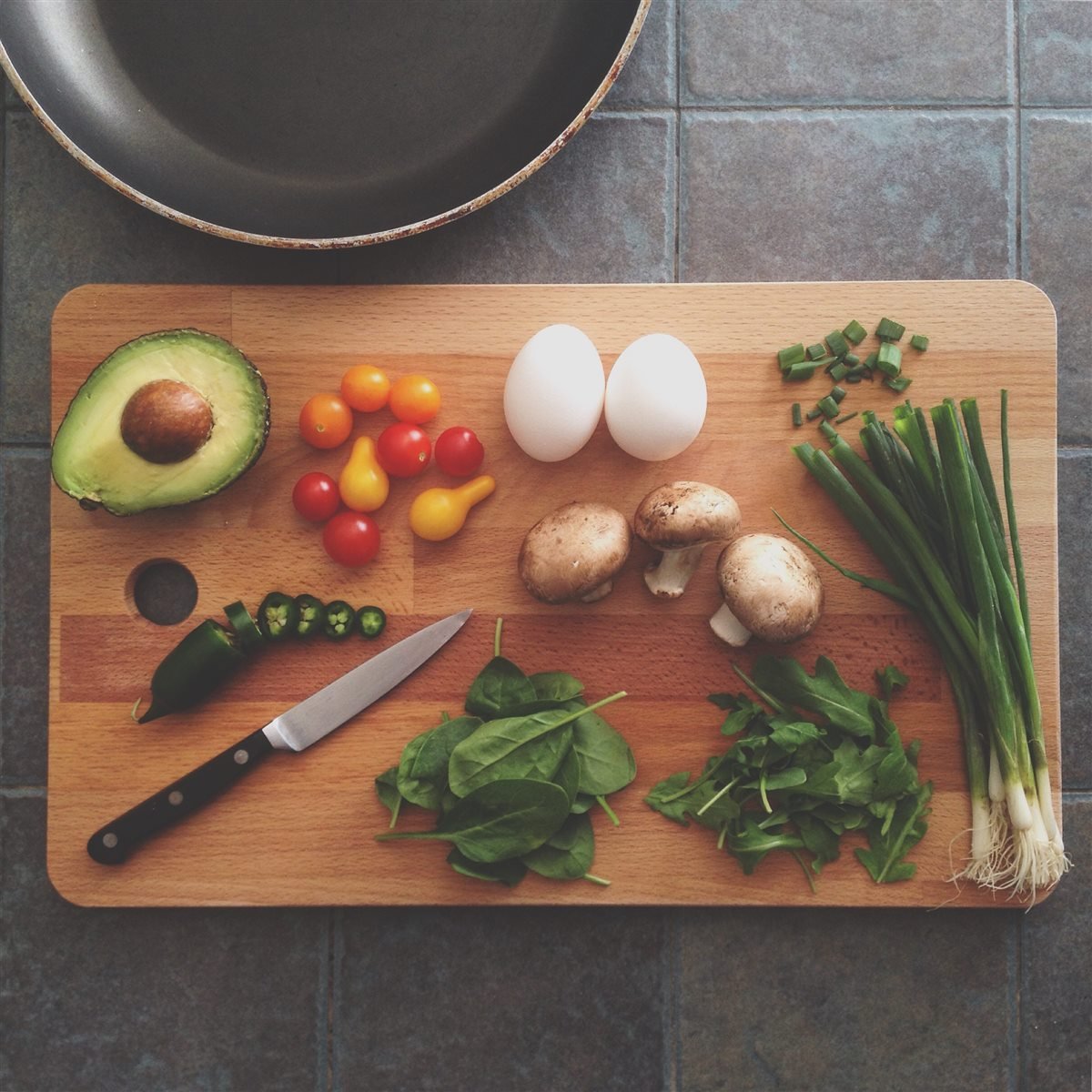 Avocado, cherry tomatoes, eggs, mushrooms, spinach, arugula and spring onions on a wooden cutting board